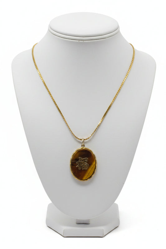 An oval pendant necklace featuring a polished tiger's eye stone with a gold Chinese character '福' (fortune) in the center, suspended from a gold chain against a white background.